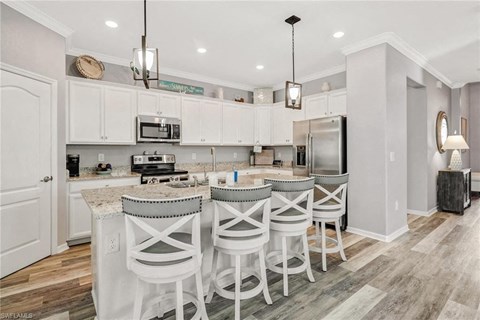 a kitchen with white cabinets and a bar with chairs
