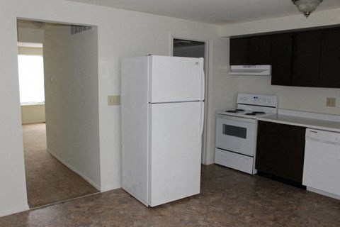 A white refrigerator stands in a kitchen with brown flooring.