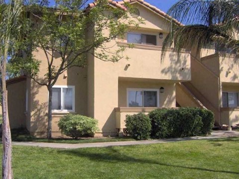A beige two-story apartment building with a tree in front.