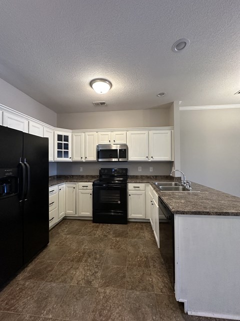 an empty kitchen with white cabinets and black appliances