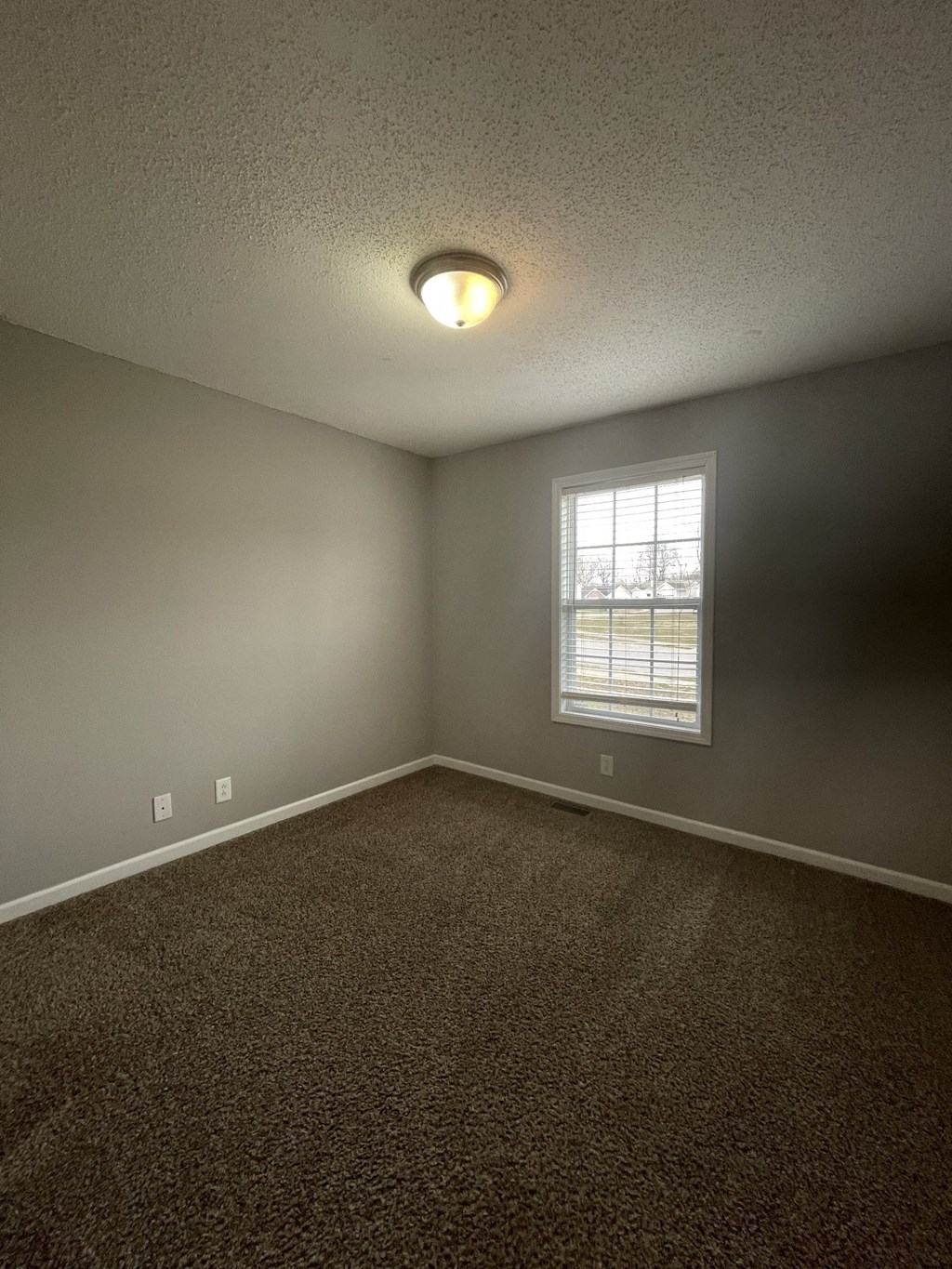 A room with a carpeted floor and a window with blinds.