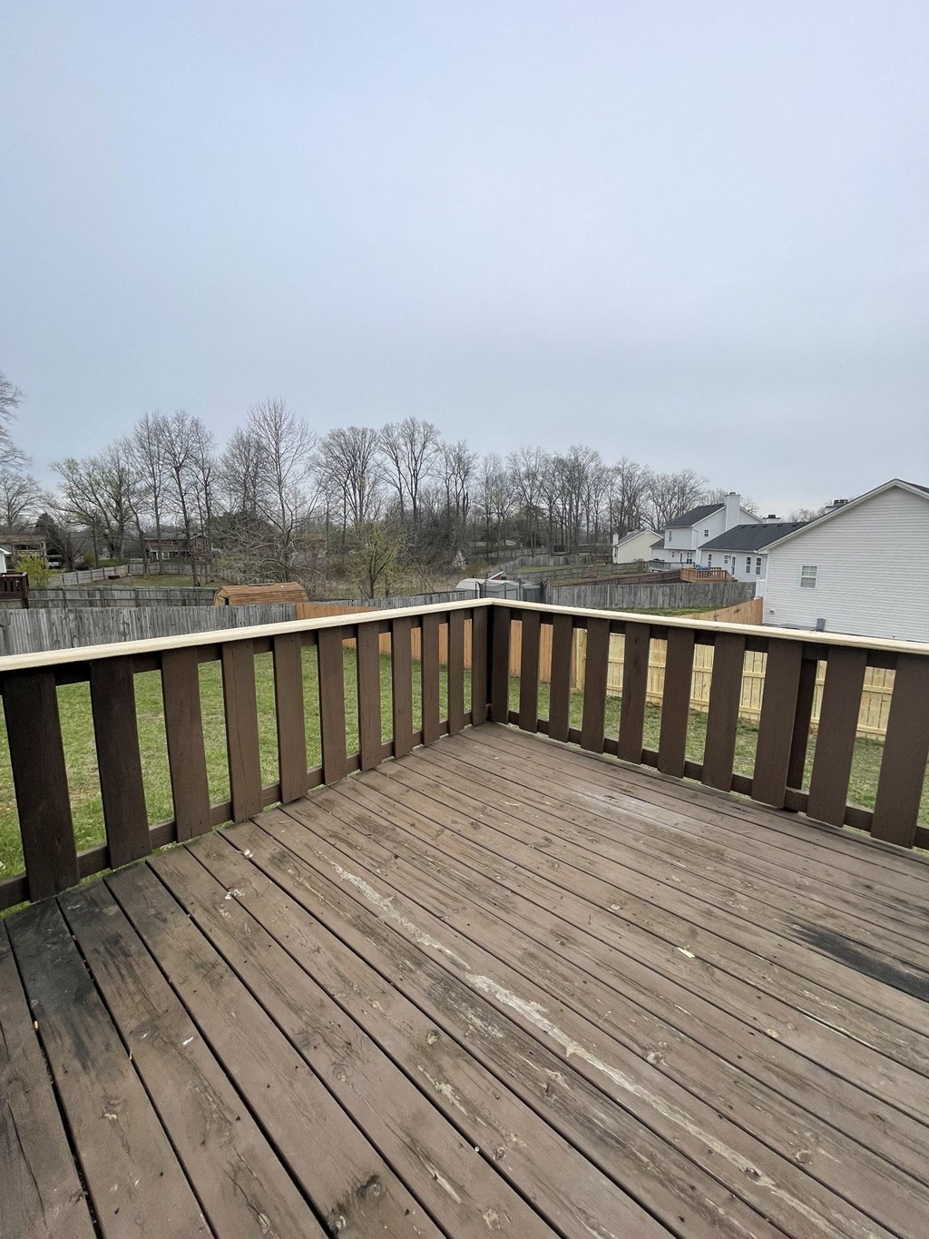 A wooden deck with a white railing and a view of a residential area.