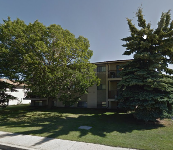 an apartment building with a lawn and trees in front of it