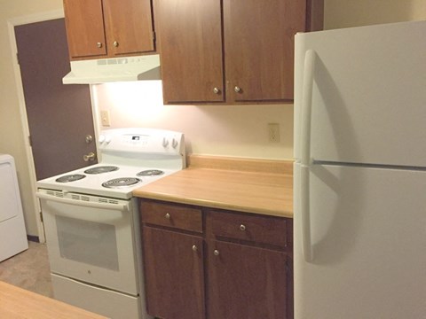 A white refrigerator stands in a kitchen with wooden cabinets.