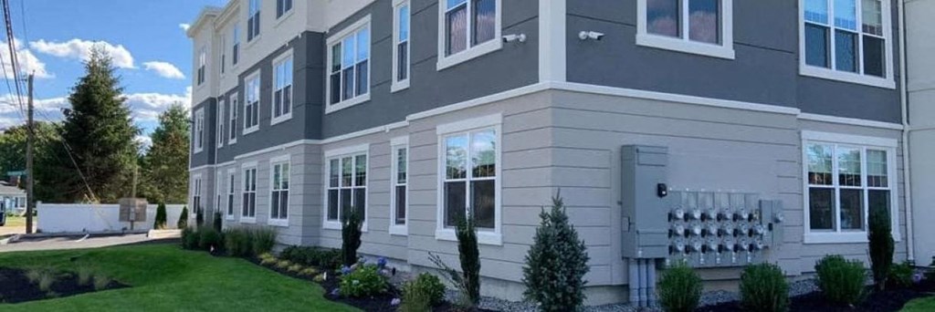 a gray and white building with green grass and trees