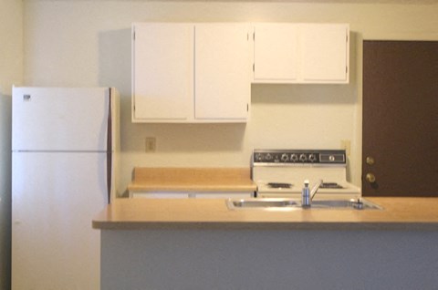 A kitchen with a white refrigerator and white cabinets.