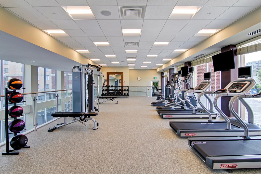 a spacious fitness room with cardio equipment and windows