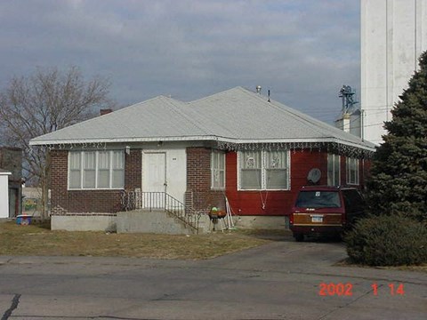 A house with a red brick exterior and a grey roof with a car parked in front.