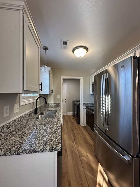 A kitchen with a granite counter top and a stainless steel refrigerator.