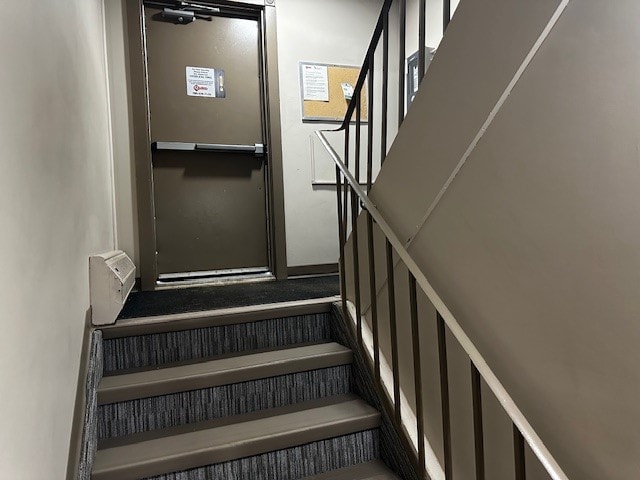 A staircase with a metal railing and a black carpeted stair tread.