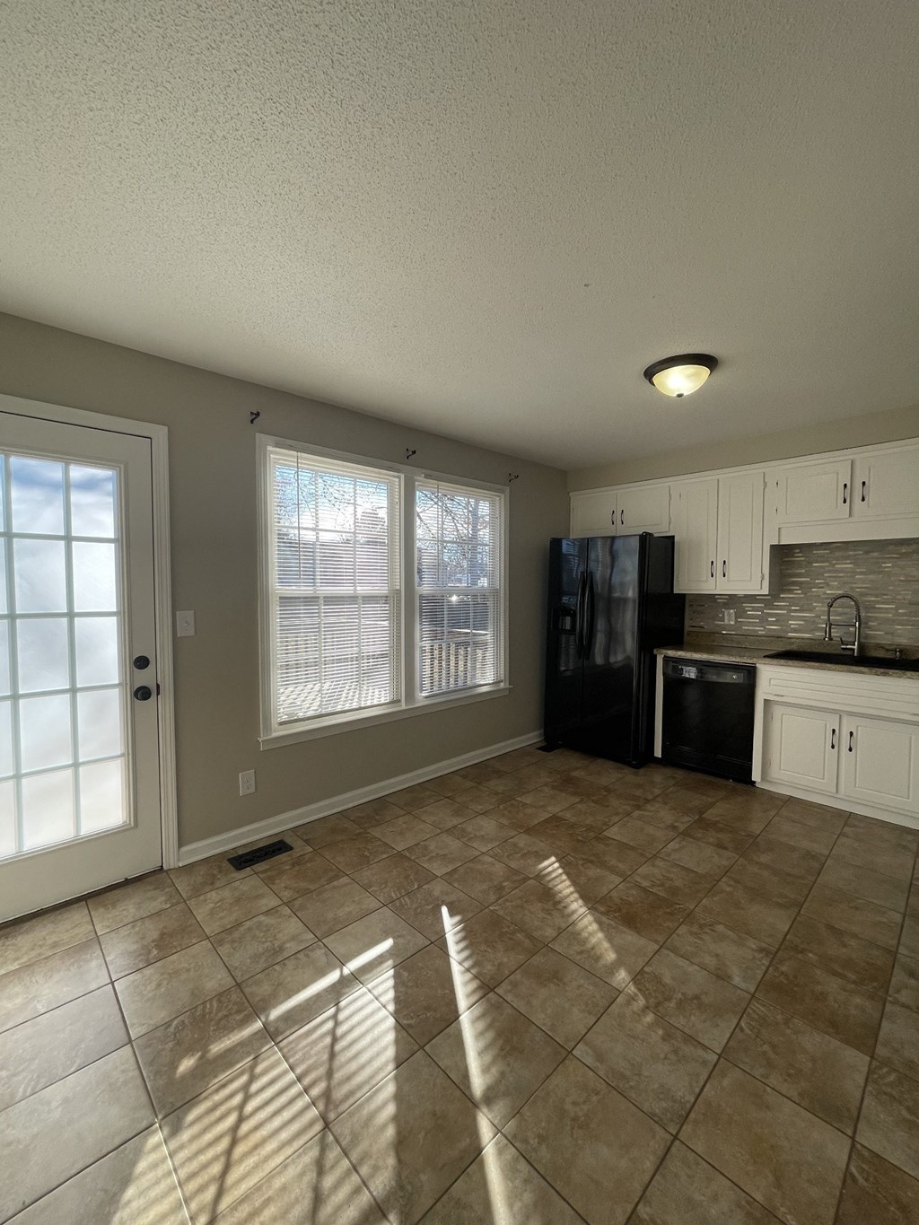 A kitchen with a black refrigerator and white cabinets.