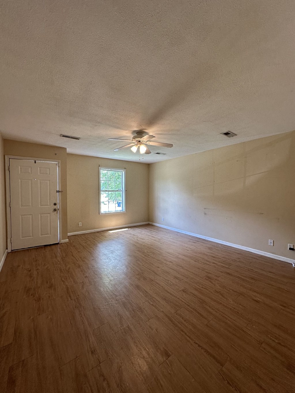 an empty living room with wood floors and a ceiling fan