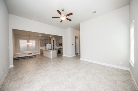 an empty living room with a ceiling fan and a kitchen