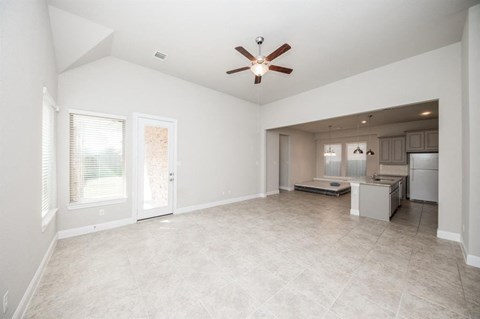 an empty living room with a ceiling fan and a kitchen