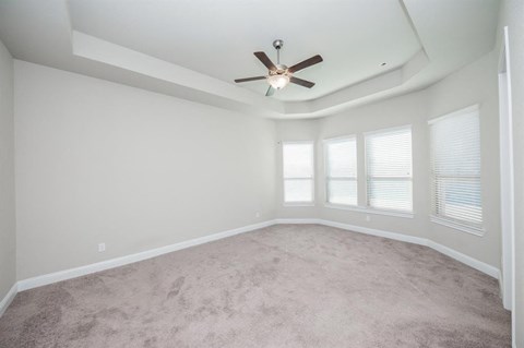 an empty living room with a ceiling fan and windows