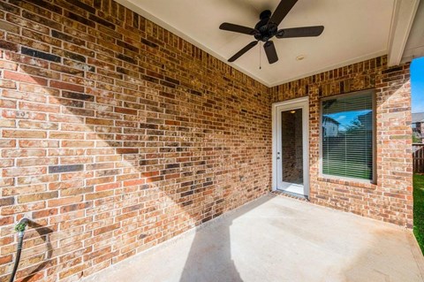 the porch of a brick house with a ceiling fan