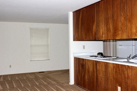A kitchen with wooden cabinets and a window with blinds.
