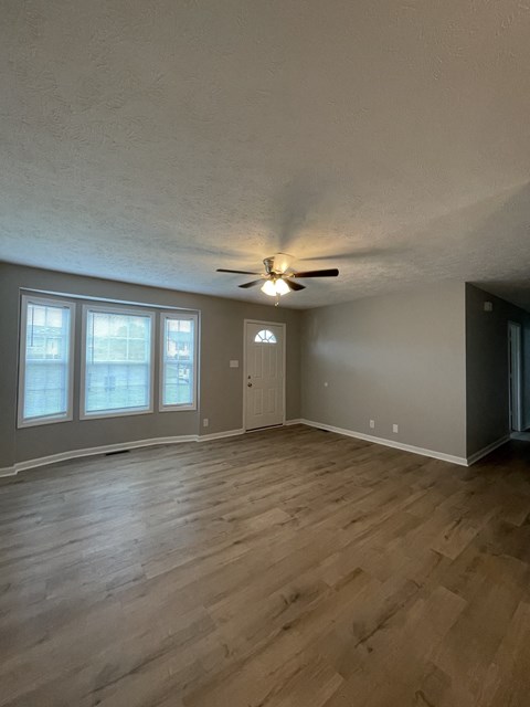 an empty living room with wood floors and a ceiling fan