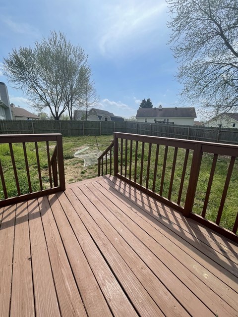 A wooden deck with a railing and a view of a grassy area and houses in the background.