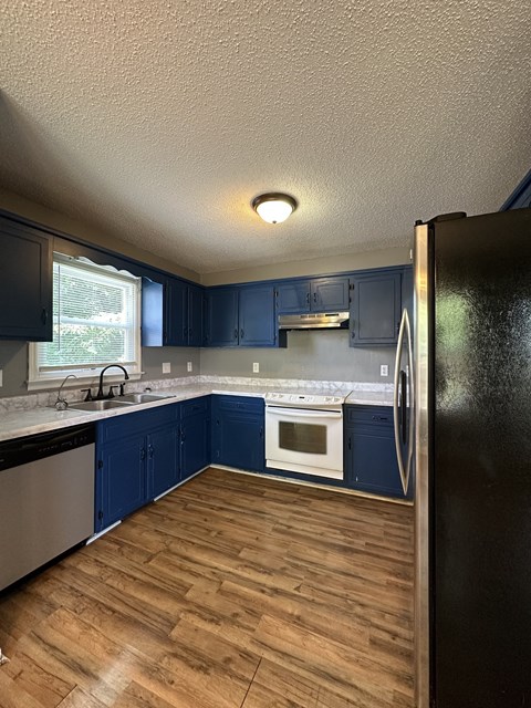 A kitchen with blue cabinets and a black refrigerator.