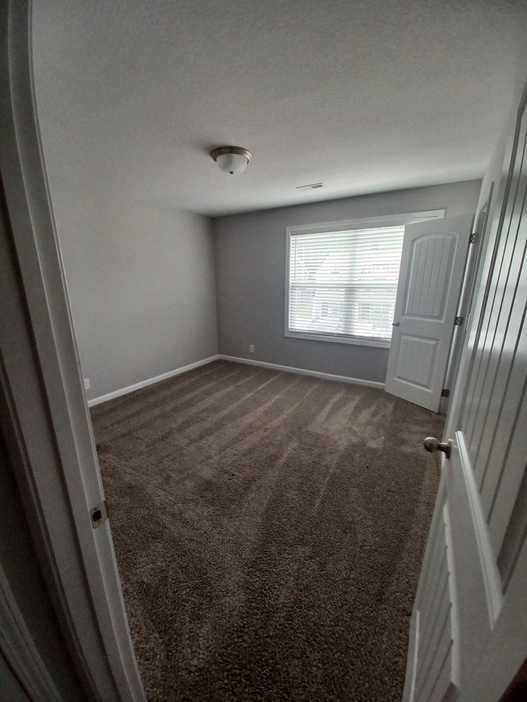 A room with a carpeted floor and a window with blinds.