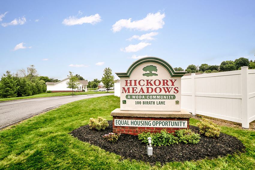 the sign for hickory meadows in front of a white fence and grass