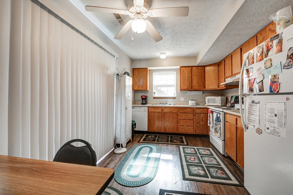 a kitchen with white appliances and wooden cabinets and a ceiling fan