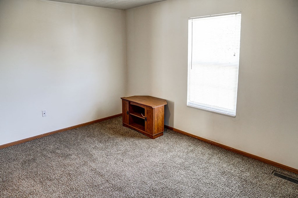 an empty room with a small cabinet and a window