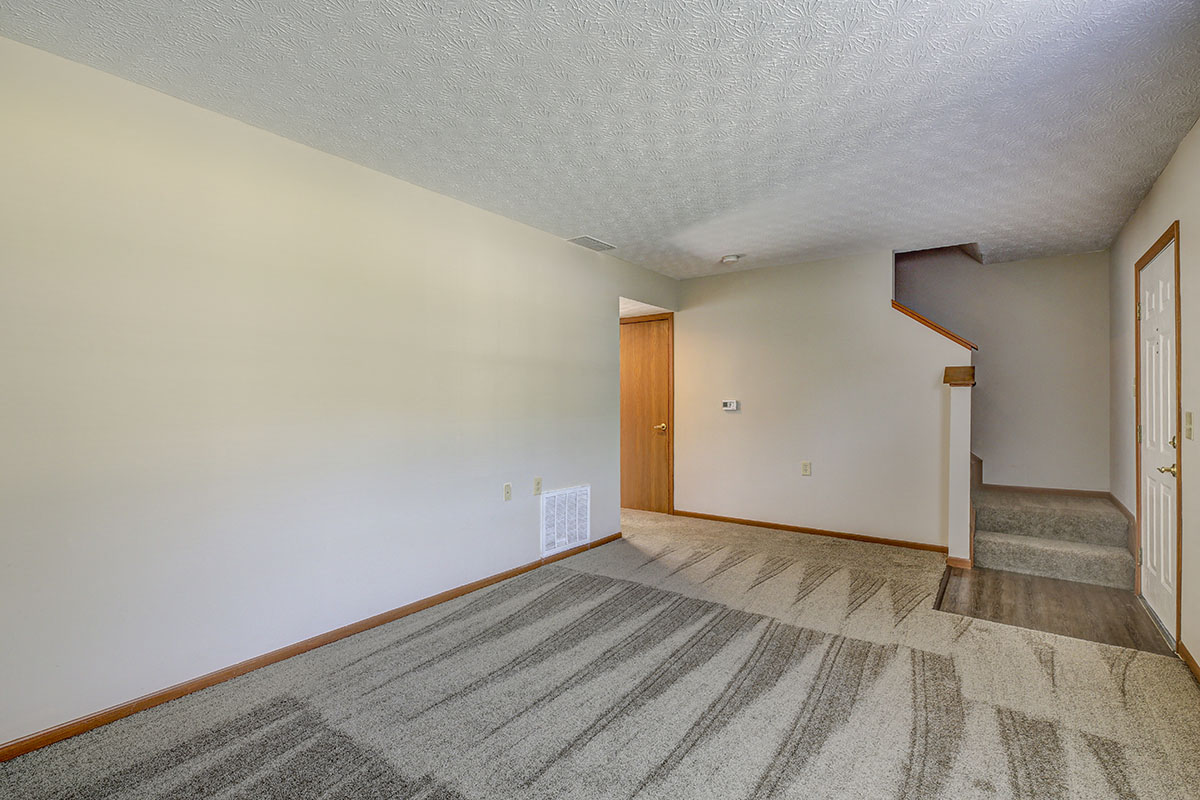 the living room and entryway of a house with carpet and white walls