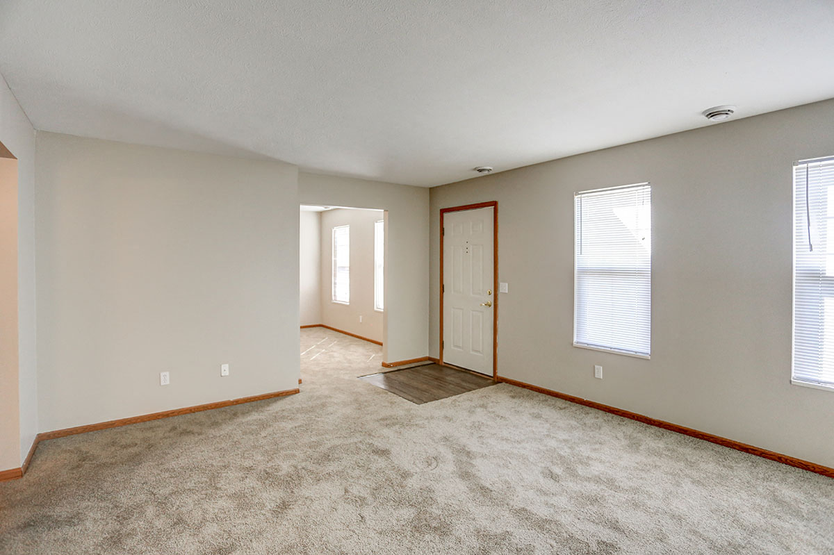 a spacious living room with carpet and a door to a hallway