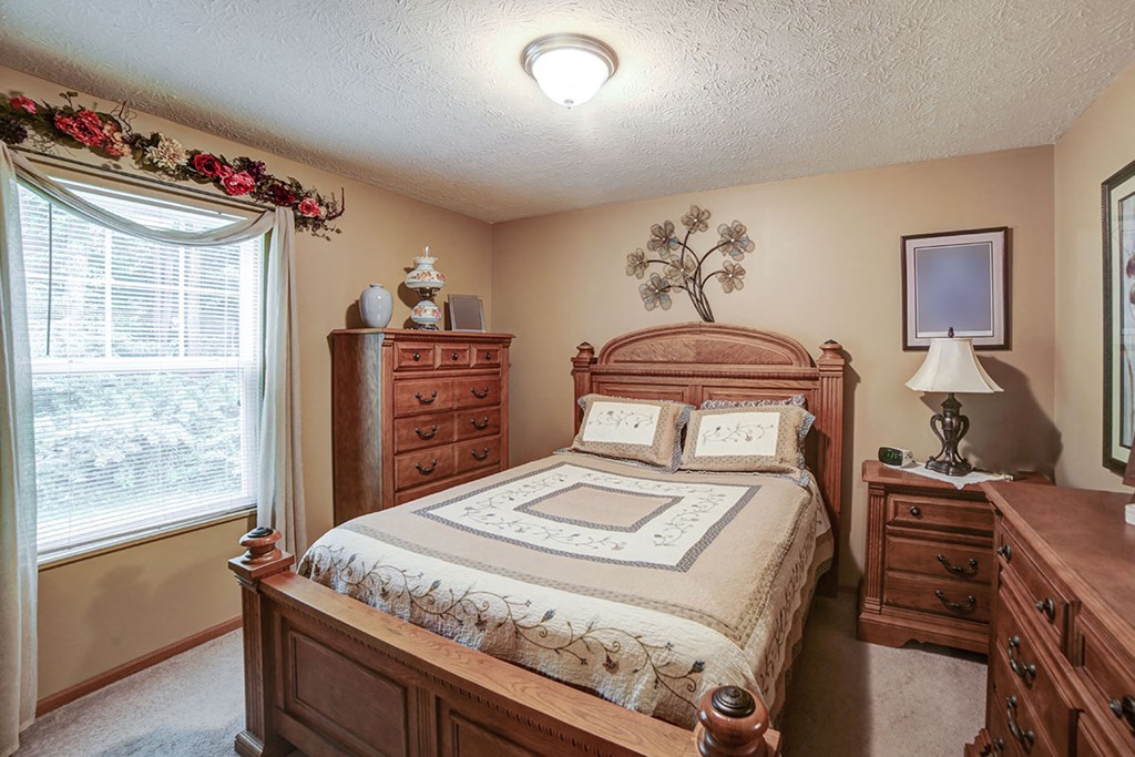 a bedroom with a bed and two dressers and a window