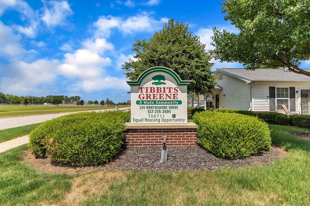 the sign is in front of a building with a lawn and bushes
