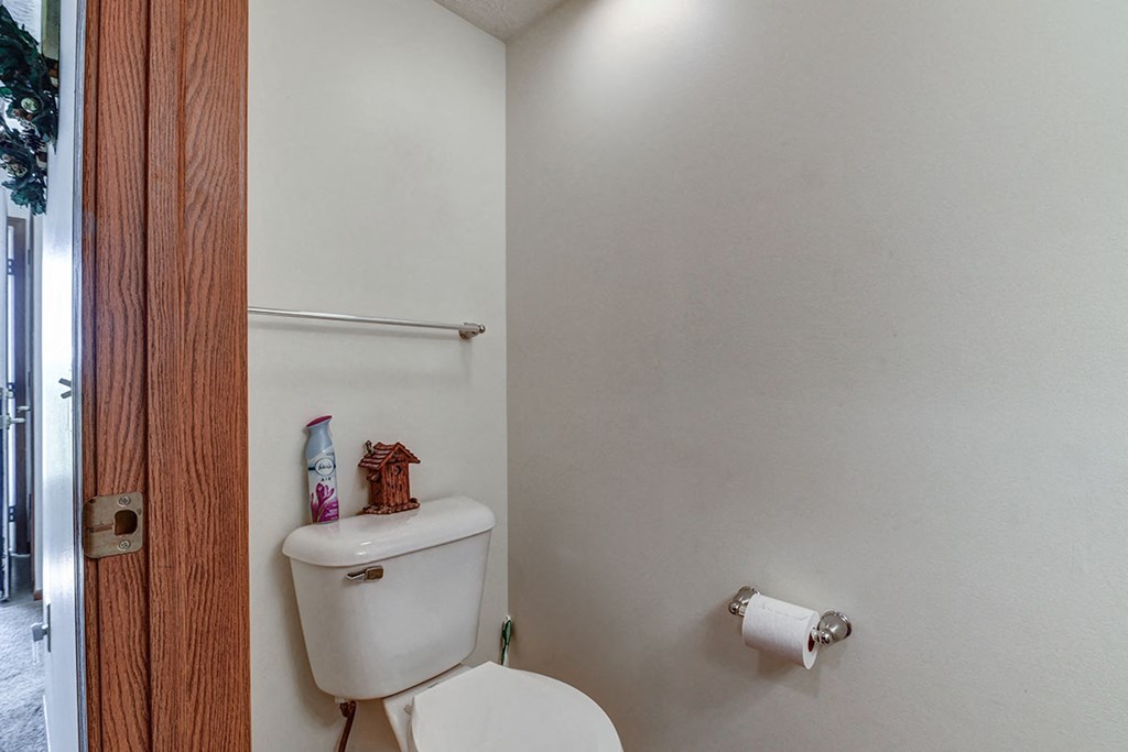 a white bathroom with a toilet and a roll of toilet paper