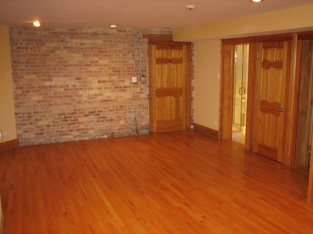 an empty living room with wood floors and a brick wall