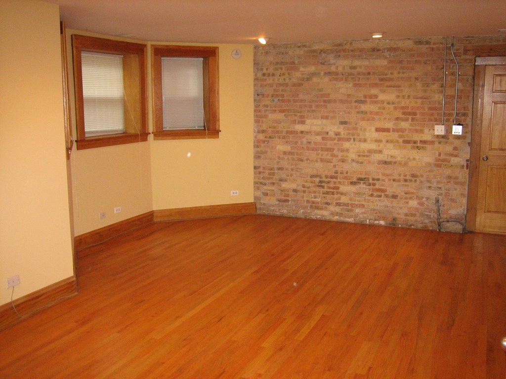 an empty living room with wood floors and a brick wall