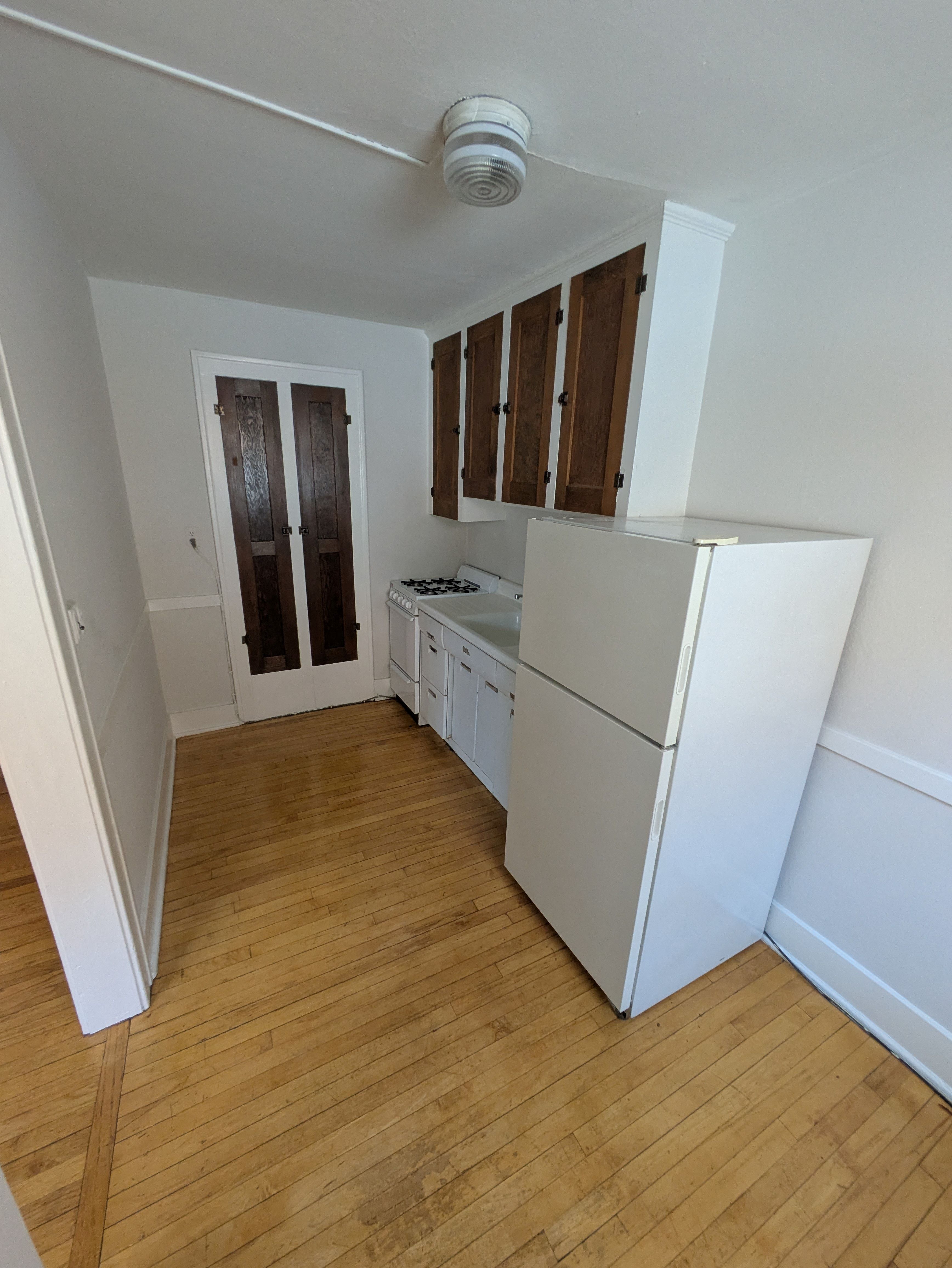 A kitchen with white appliances and wooden floors.