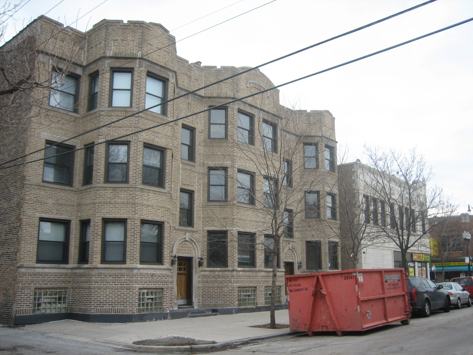 a large brick apartment building with a red dumpster on the street