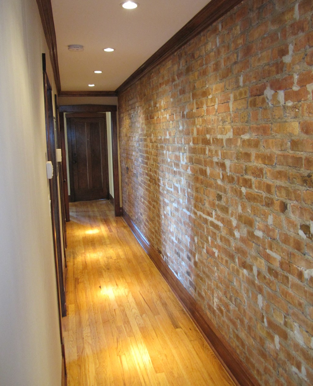 an exposed brick wall in a hallway with wooden floors