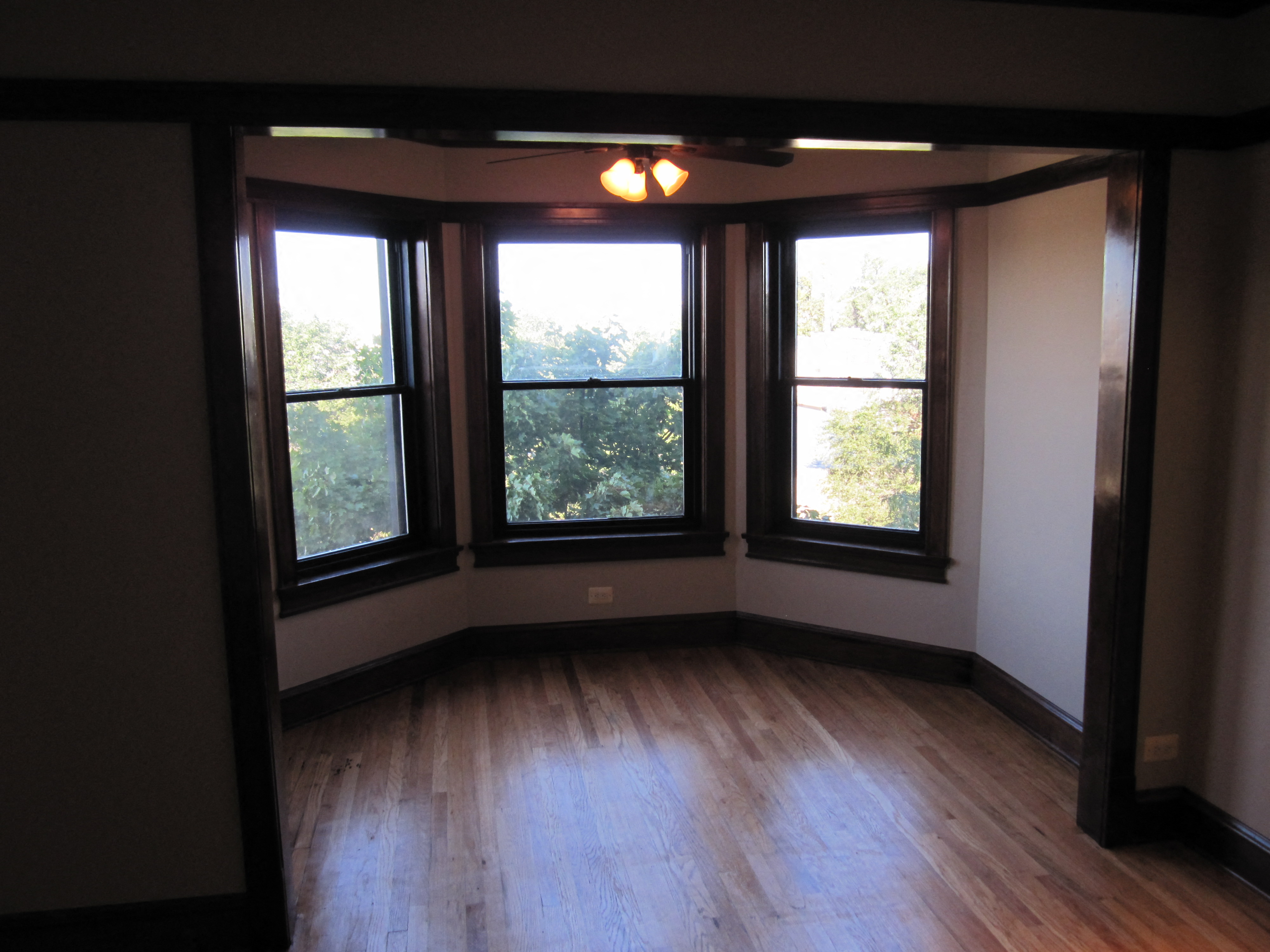 an empty living room with three windows and wood floors