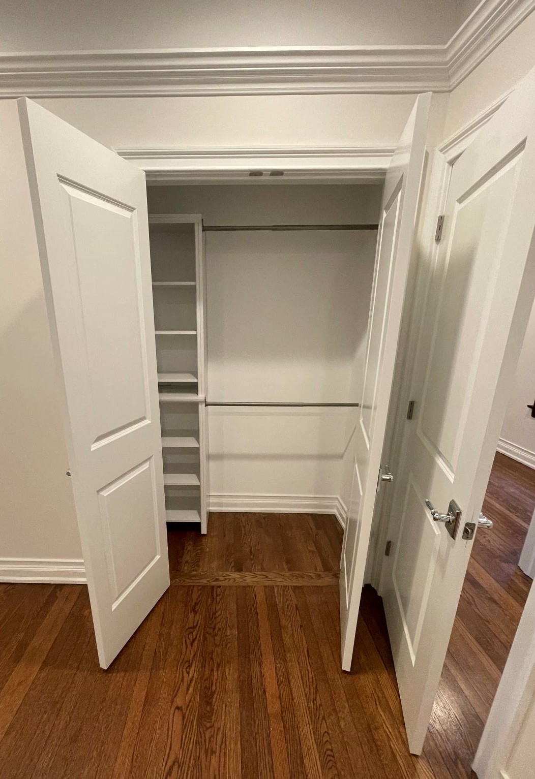 a walk in closet with white doors and a wood floor