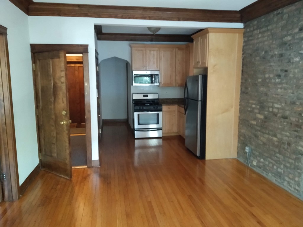 an empty living room with wooden floors and a kitchen with stainless steel appliances
