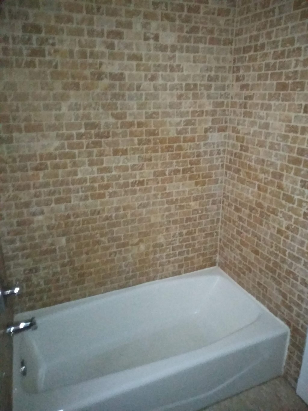 a bathroom with a white tub and a brick wall
