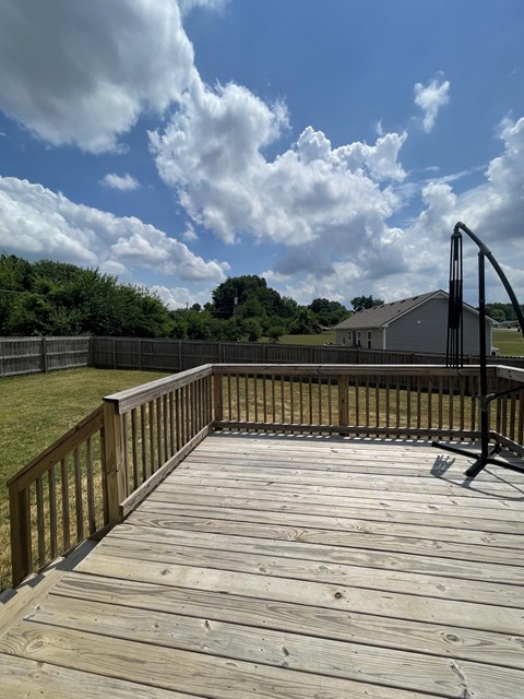 A wooden deck with a black railing and a small building in the background.