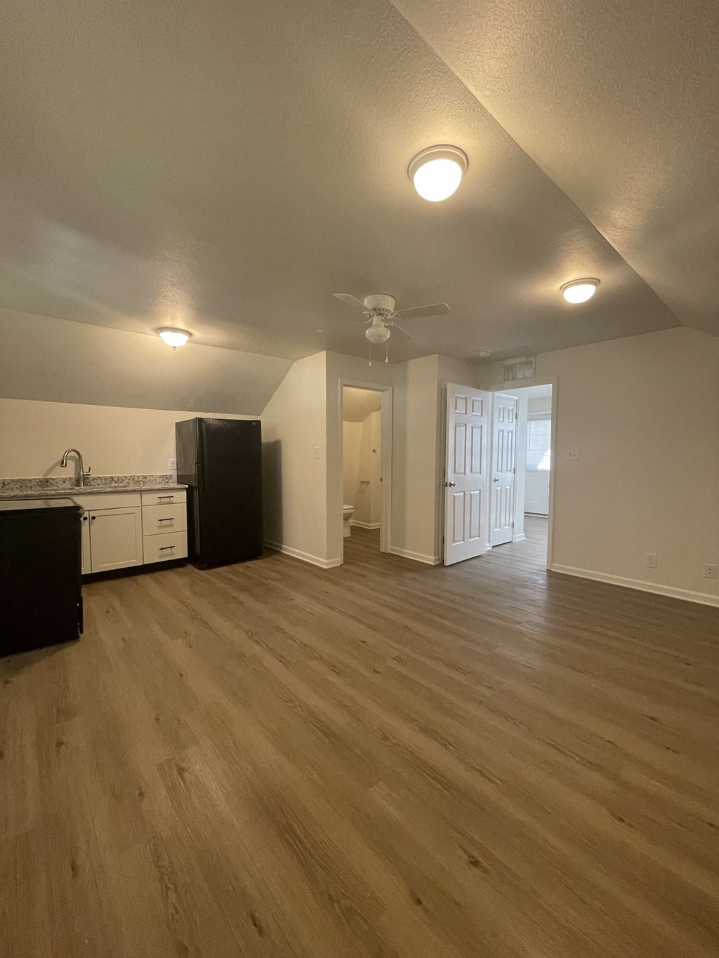 an empty living room with a kitchen and a ceiling fan