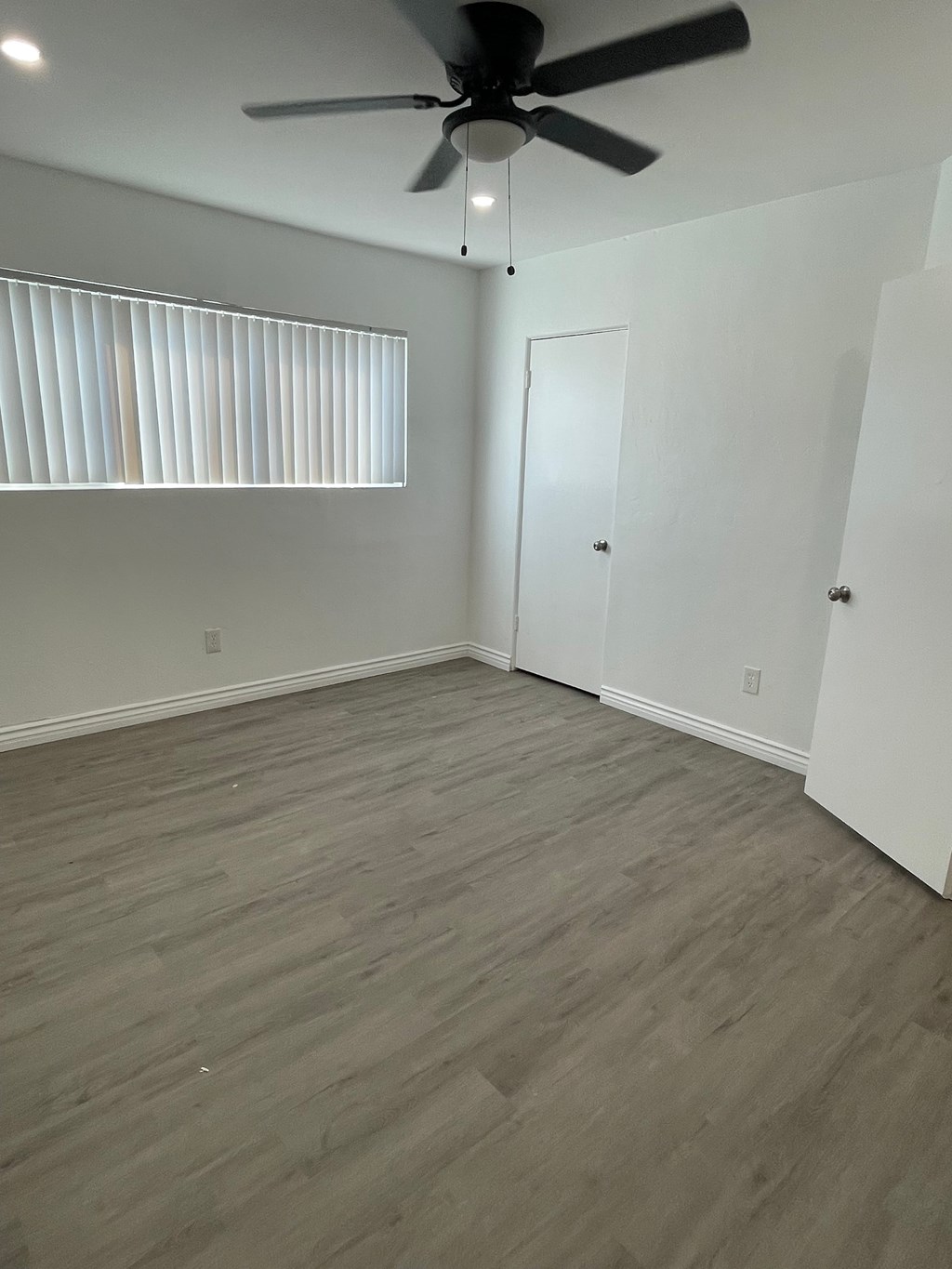 A room with a ceiling fan and a window with blinds.