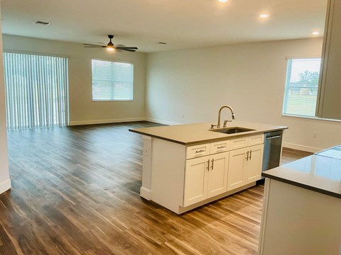 an empty living room with a kitchen and a ceiling fan