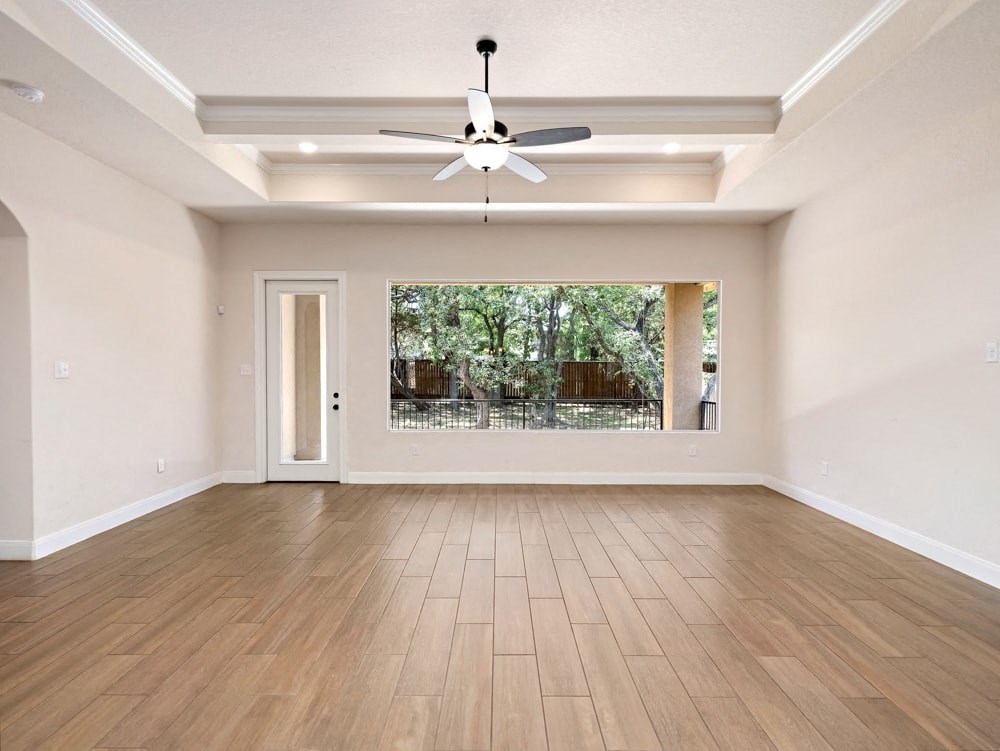 an empty living room with a large window and a ceiling fan