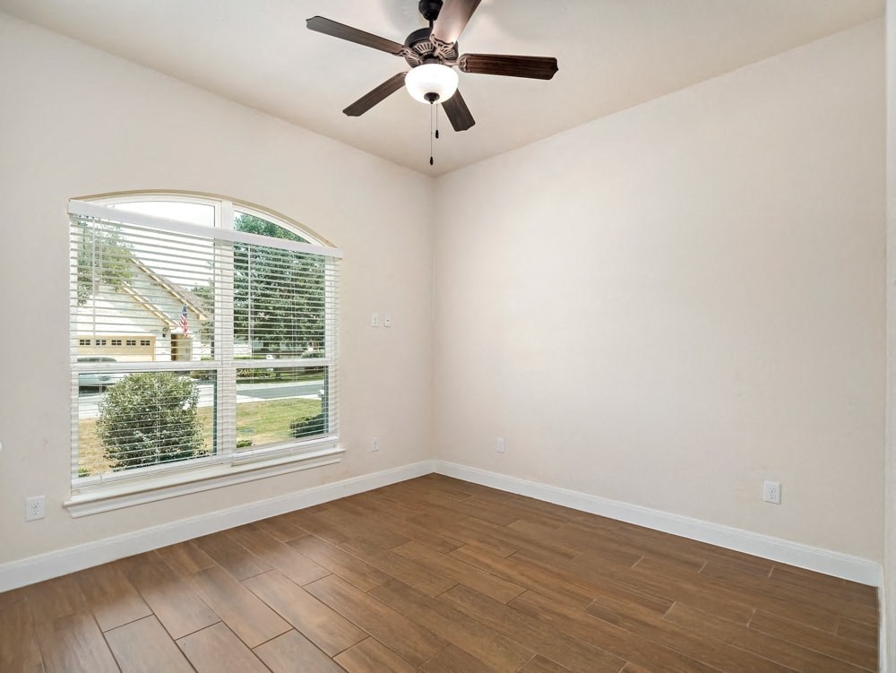 an empty living room with a large window and a ceiling fan