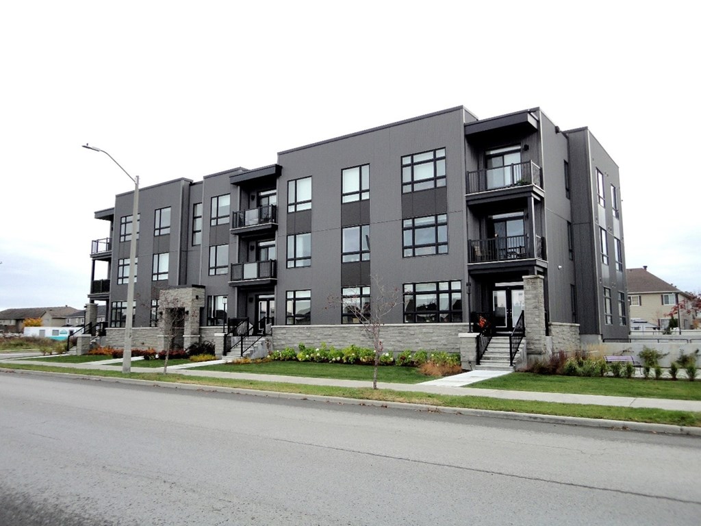 A grey apartment building with balconies and a front yard.