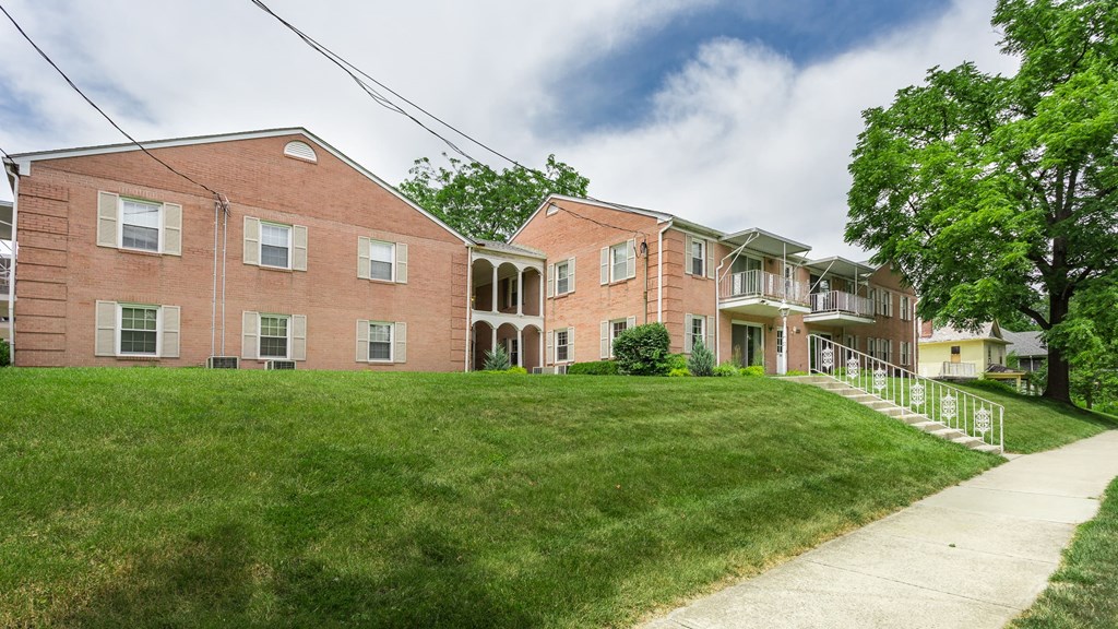 a large brick apartment building with a green lawn and a sidewalk